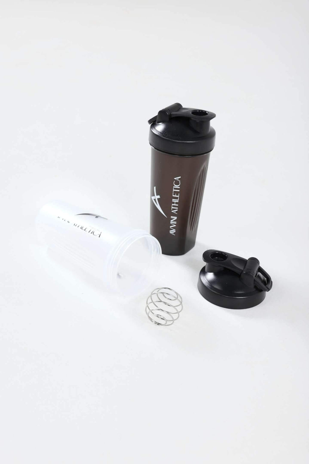 Black protein shaker bottle standing next to clear shaker bottle lying on its side with the lid and shaker ball next to it