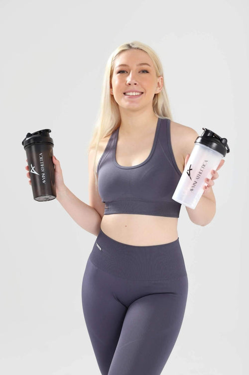 Girl smiling wearing Invictus set in charcoal holding one white and one black shaker bottle in each hand 