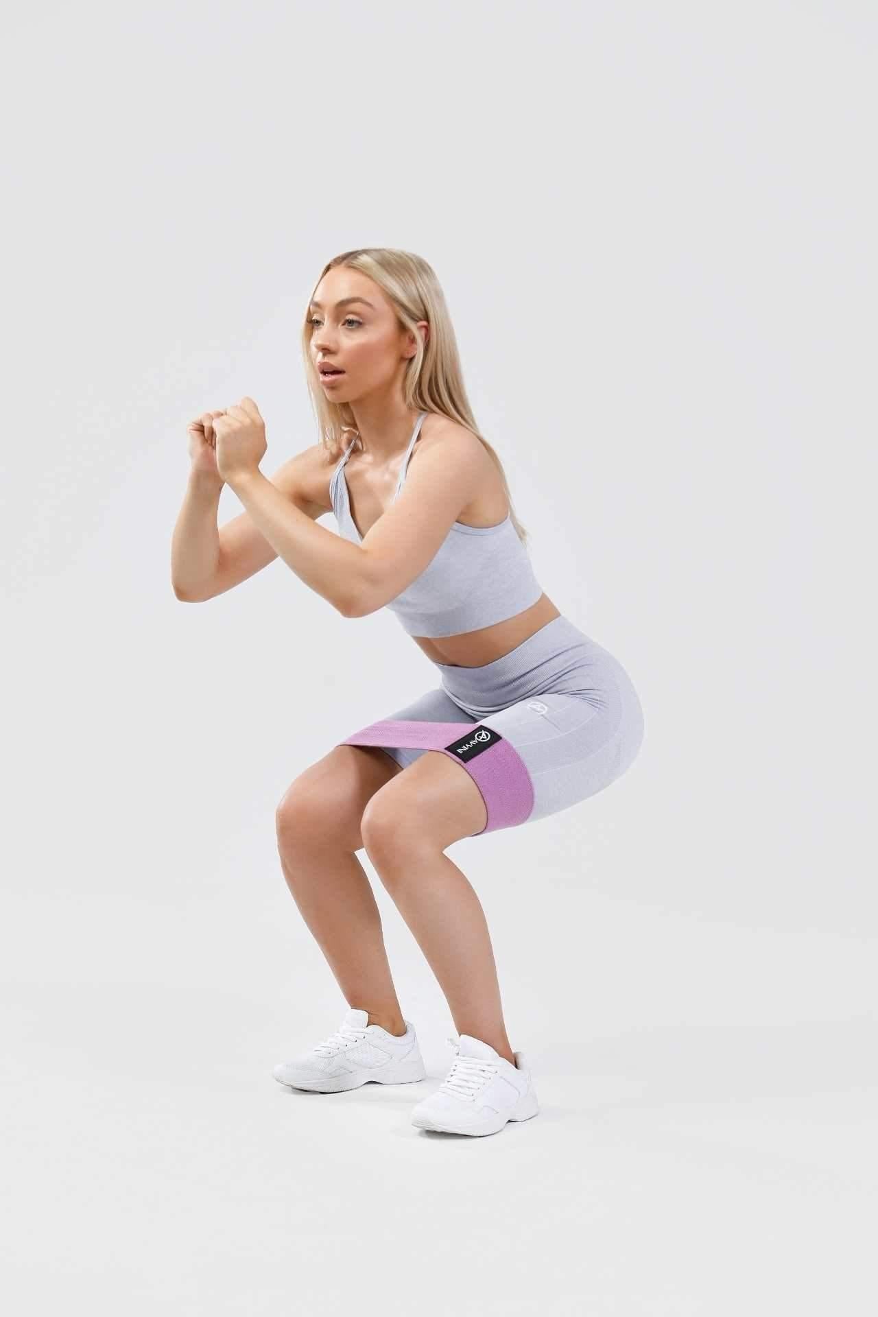 Girl holding squat in calypso seamless set in blue marl wearing purple resistance band around thighs