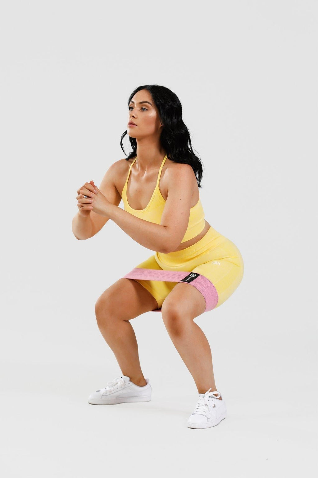 Girl squatting wearing yellow calypso seamless set, pink resistance band around thighs