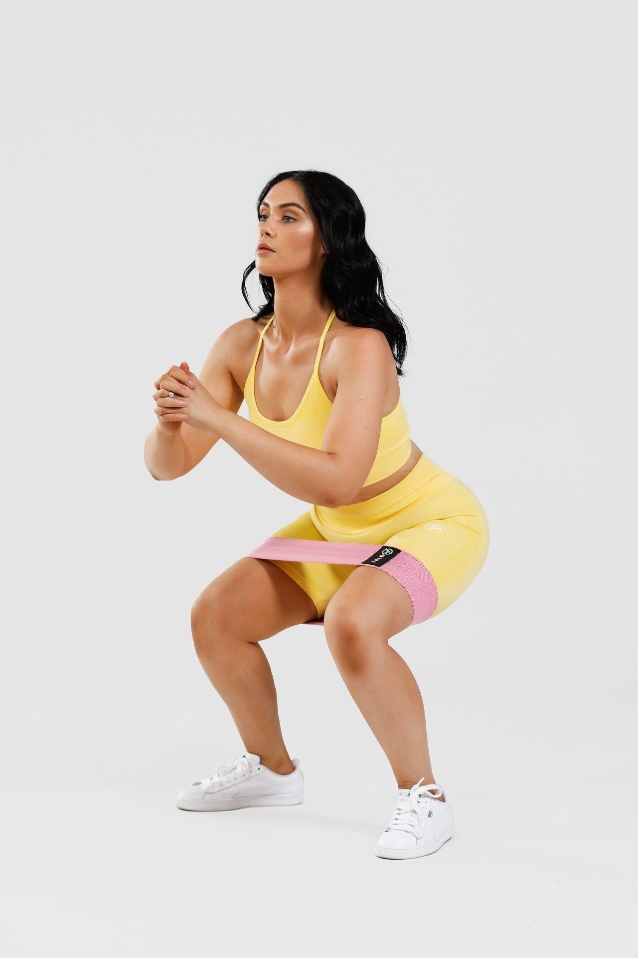 Girl squatting wearing yellow calypso seamless set, pink resistance band around thighs