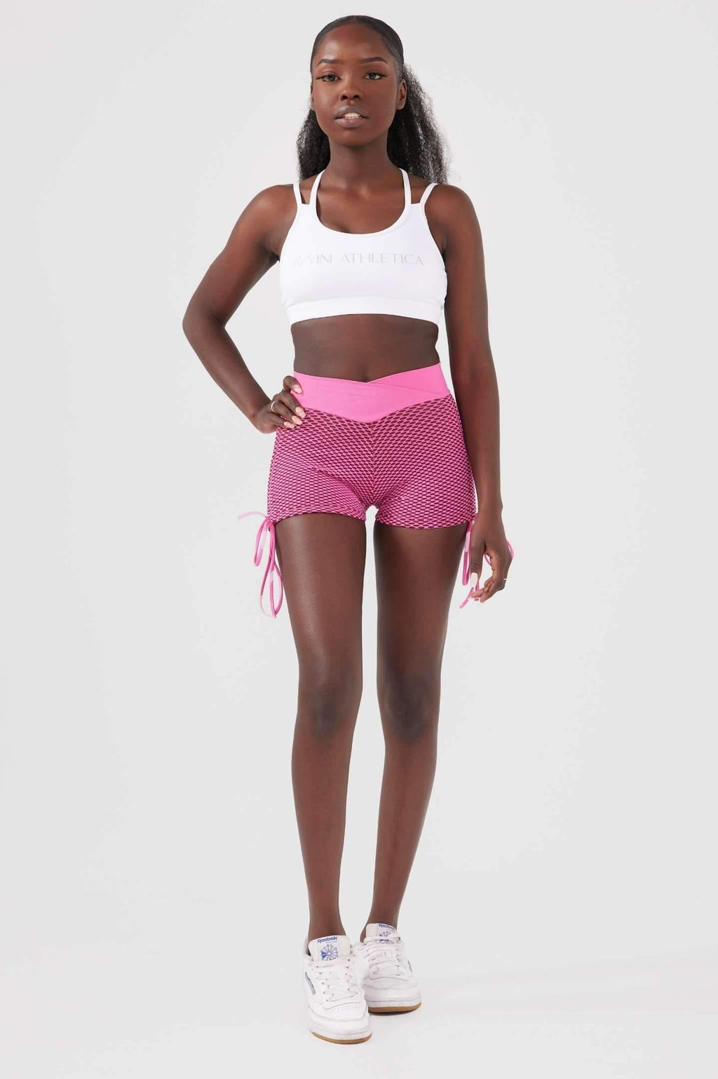 Girl wearing pink luna scrunch bum shorts hand on hip, white crop top